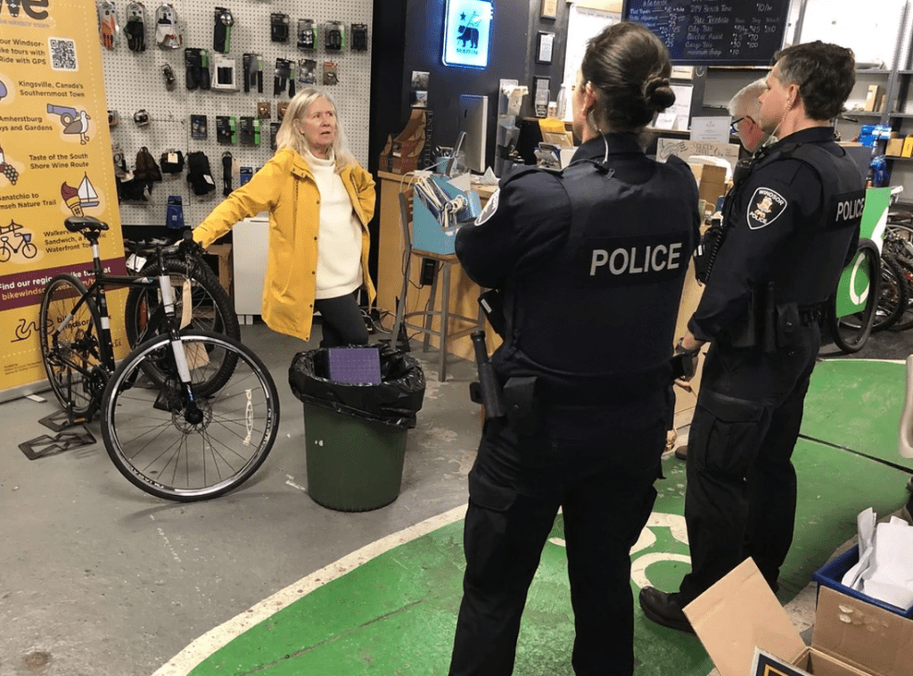 Two police officers stand in front of a woman in a yellow coat in a bicycle shop.